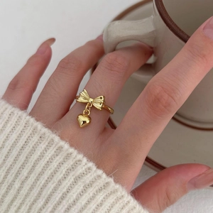 Elegant gold bow ring with heart pendant worn on hand in a cozy lifestyle setting
