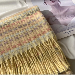 Detail shot of a soft rainbow plaid knit scarf with fluffy yellow tassels on white fabric