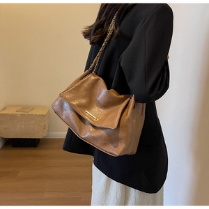 Close-up of caramel brown leather shoulder bag with gold metal buckle and chain strap