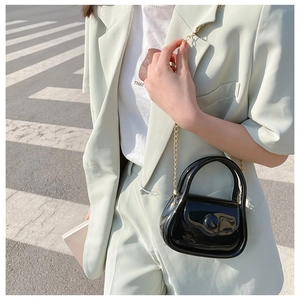 Mini glossy black patent leather bag with gold chain strap on street background