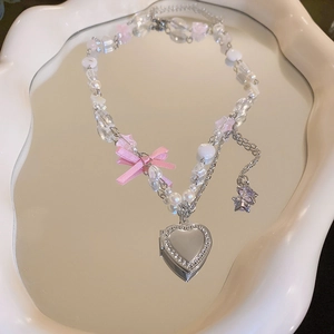 Détail du collier de perles avec nœud rose et médaillon cœur argenté sur un miroir