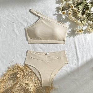 Flat lay of cream ribbed one shoulder bikini set with high waist cross design and dry flowers