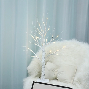 Illuminated white birch tree with warm LED lights on a cozy chair for home decor