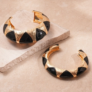Detail view of gold metal cuff with black enamel triangles and hammer-textured surface
