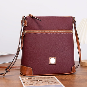Detailed view of burgundy lychee grain leather crossbody bag on a rustic wooden desk