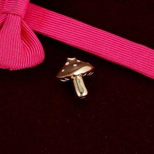 Detailed close-up of a brown mushroom alloy charm with white spots on red velvet background