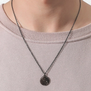 Detail of a black Tai Chi Yin Yang pendant on a model wearing a pink sweater