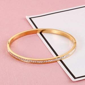 Detail of gold oval bangle featuring a row of square-cut white crystals on a pink surface