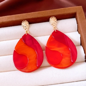 Détail de boucles d'oreilles en acrylique orange et rouge avec clous en métal doré martelé