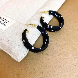 Macro shot of fabric wrapped hoop earrings with white polka dots on black material
