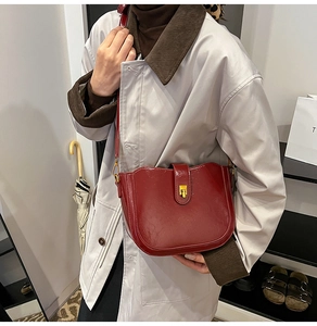 Detail of red vintage saddle bag with glossy leather texture and gold buckle on a model