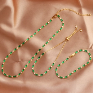 Detail of gold chain necklace and bracelet with green emerald-cut stones on pink silk