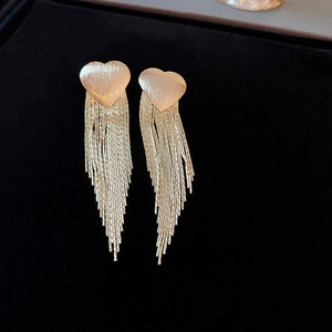 Detail of elegant gold tassel earrings with heart-shaped stone on black velvet background