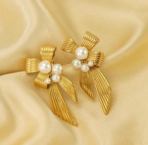 Detail of vintage gold bow earrings with white pearls on elegant champagne silk fabric