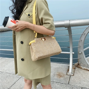 Close-up of beige woven straw beach bag with yellow leather handle and gold twist lock