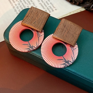 Macro view of geometric wood earrings featuring red sunburst and black bamboo leaf patterns