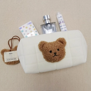 Quilted white cosmetic bag featuring a plush bear head and hanging name tag with accessories