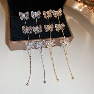Détail de boucles d'oreilles nœud en zircon avec longues chaînes à pompons sur un écrin