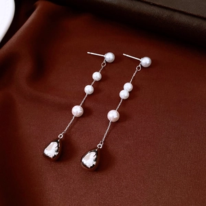 Macro shot of French vintage pearl drop earrings featuring silver tassels on silk fabric