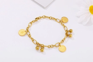 Dettaglio del bracciale dorato con ciondoli moneta Elizabeth II e sfere tonde