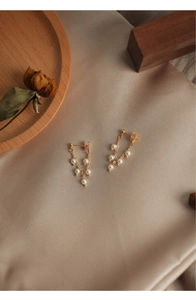 Detail shot of golden tassel earrings with white freshwater pearls on champagne silk