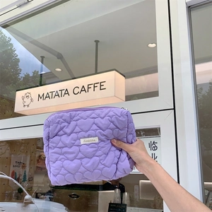 Close-up of light purple quilted makeup bag with heart patterns and brand label