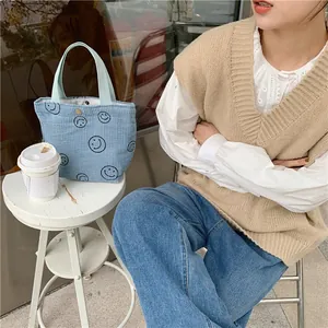 Close-up of a blue corduroy tote bag with black smiley faces used in an outdoor setting