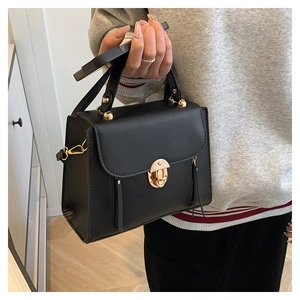 Close-up of matte black leather handbag featuring golden semi-circle lock and metal studs
