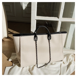 Detail of canvas tote bag with black leather trim and silver chain shoulder strap