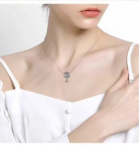 Detail of silver necklace with hollow round pendant and a small green gemstone on model