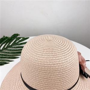 Detail of light brown woven straw hat featuring a pink fabric flower and black ribbon accent