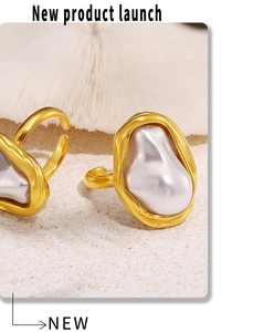 Close-up of golden titanium steel rings with irregular baroque pearls on beach sand