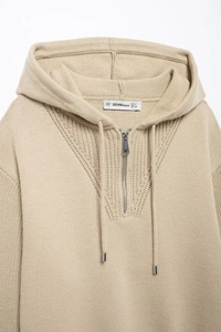 Detail of beige knit hoodie collar with half-zipper, drawstring, and size label