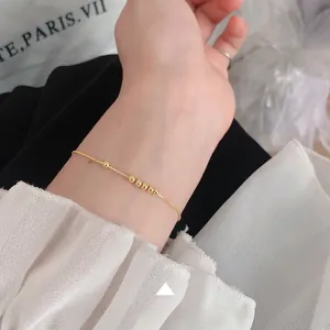 Detailed close-up of a minimalist gold bead bracelet worn on a woman's wrist