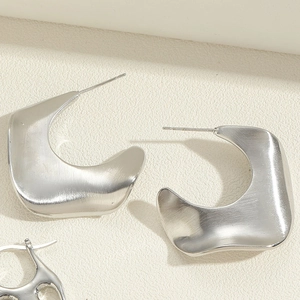 Detailed shot of asymmetric matte silver earrings with a brushed metallic texture finish