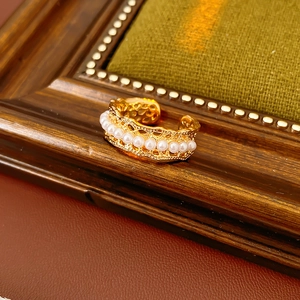 Detail of vintage hollow lace pearl ring with warm gold finish on a wooden frame
