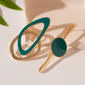Boucles d'oreilles asymétriques en or et émail vert foncé sur un support minimaliste