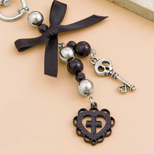 Detail of keychain featuring black ribbon bow, silver skull key and dark heart cross charms