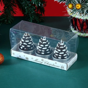 Close-up of three pinecone candles with snow effect in a clear Merry Christmas gift box