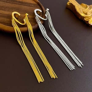 Detail of elegant gold and silver tassel ear cuffs with long chains on a textured surface