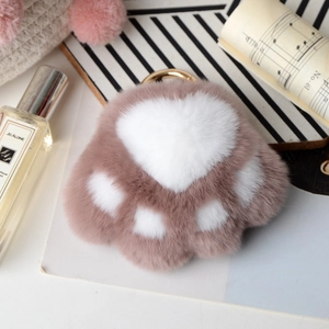 Macro detail of a soft dusty pink plush cat paw keychain with golden metal hook