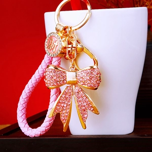 Detail of pink crystal bow keychain with gold finish and lucky charm on braided strap
