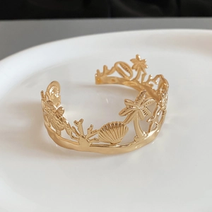 Macro detail of golden starfish open bracelet with embossed sea life and palm tree patterns