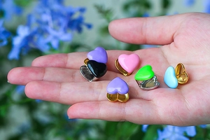 Macro shot showing small colorful heart earrings in various pastel colors on a hand