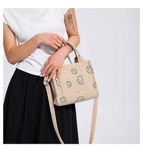 Detail of corduroy shoulder bag in beige featuring a minimalist black smiley face pattern