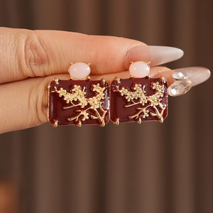 Detail of vintage enamel earrings with red base, gold floral branch, and pink gemstone