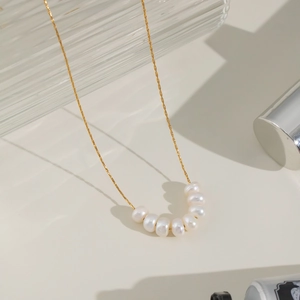 Elegant gold chain necklace featuring natural white baroque pearls on a beige surface