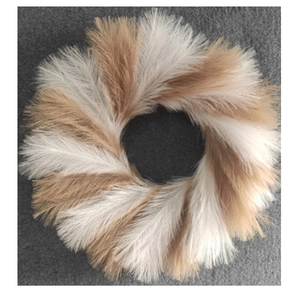 Top view of faux reed Christmas wreath with white and light brown feathers on grey fabric