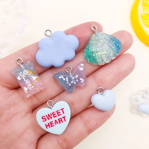 Blue resin pendants set with butterfly shell and candy charms held in palm