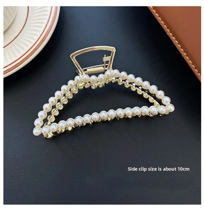 Detail view of large gold-tone pearl hair claw clip on black leather surface, size 10cm